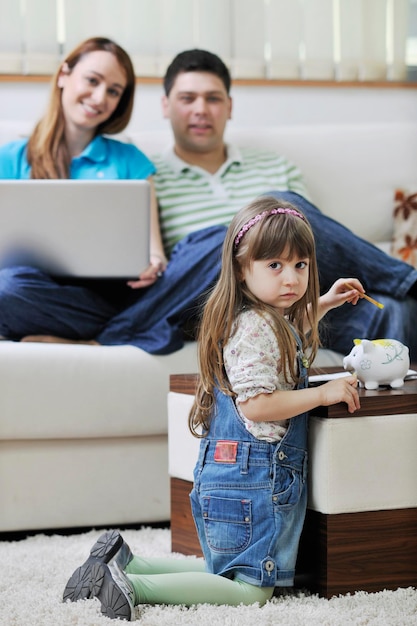 young happy family at bright and modern living room puting money in piggy bank and working on laptop computer on home finance