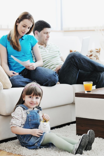 young happy family at bright and modern living room puting money in piggy bank and working on laptop computer on home finance