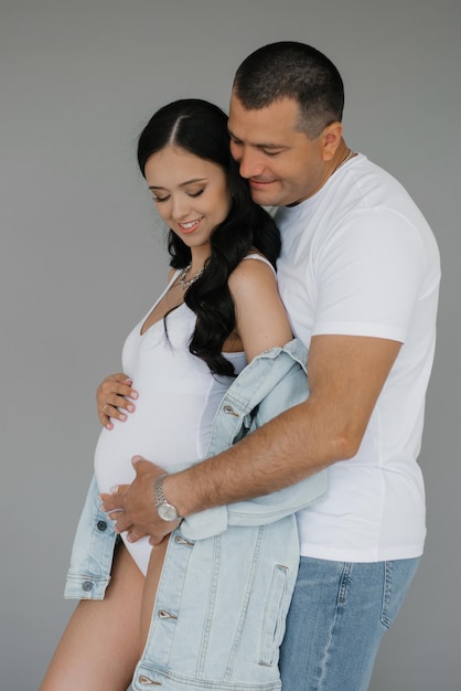 A young happy family husband and wife are expecting a baby A man embraces a pregnant woman on a gray background