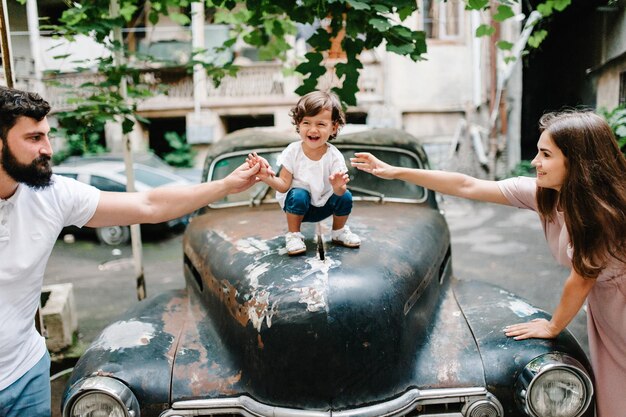 Young happy family mother father baby daughter during a walk the streets near ancient vintage car of the old city town outdoors The concept of family holiday and travel