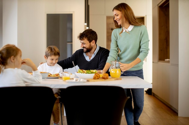 Young happy family talking while having breakfast at dining table at apartment