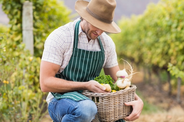 Young happy farmer holding a basket of vegetables