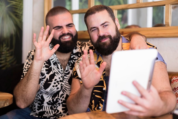 Young happy gay couple making a video call from a tablet Concept of remote connections