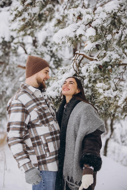 A young happy and loving couple is standing under a pine tree from which snow falls in winter