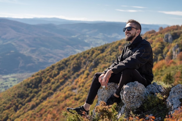 A young happy man enjoying in view on the mountain top a male smiling hipster relaxing in nature