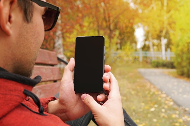 Young happy man holds in his hand his smartphone and shows the screen Technology and people use smartphone outdoors in the open air