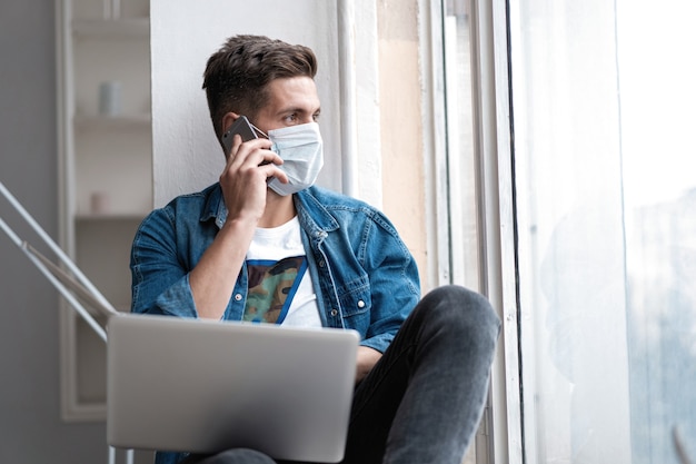 Young happy man sitting in protective mask talking on the phone.