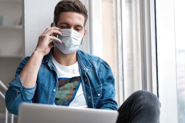 Young happy man sitting in protective mask talking on the phone.