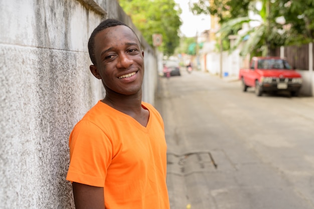 Young happy man smiling while thinking and leaning against old cement wall in the streets outdoors