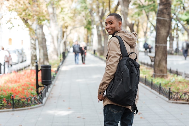 Young happy man wearing backpack walking on the street while holding book