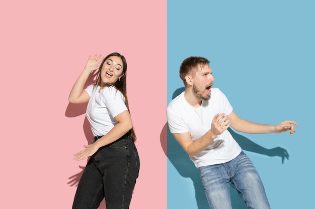 Young and happy man and woman in casual clothes on pink and blue bicolored wall