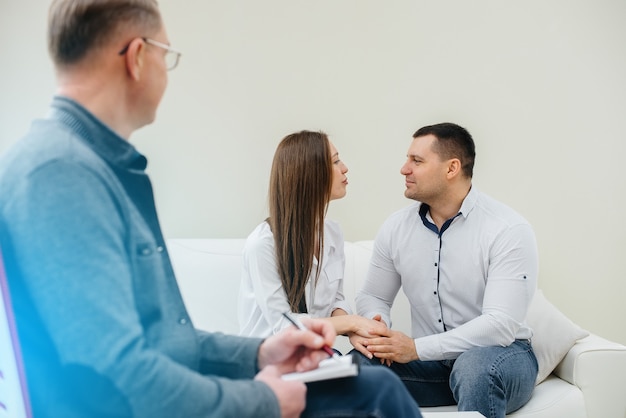 A young happy married couple of men and women talk to a psychologist at a therapy session. Psychology.