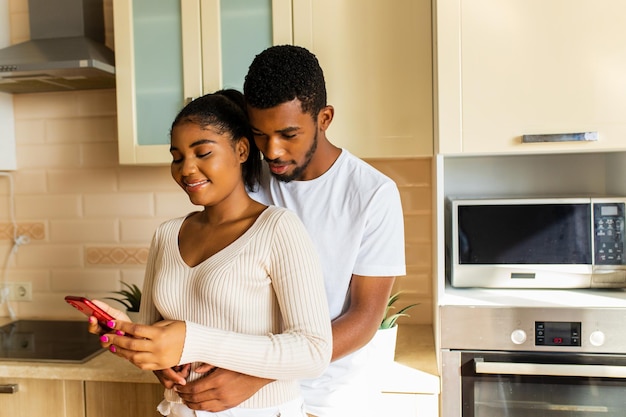 Young happy mixed race couple looking at smartphone screen at home in the kitchen