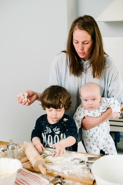 Young and happy mom with her children in the kitchen cook cookie dough or cake