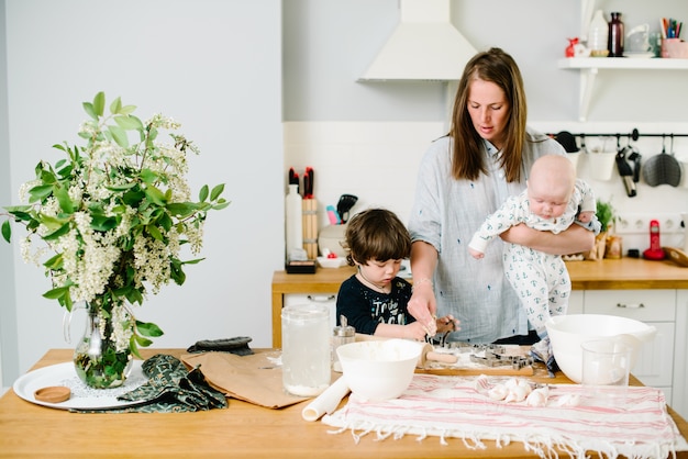 Young and happy mom with her children in the kitchen cook cookie dough or cake