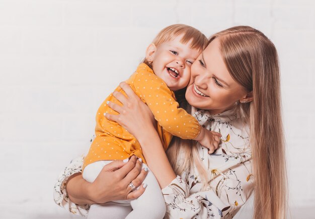 A young happy mother hugs her baby daughter against a bright background. Mother-child communication