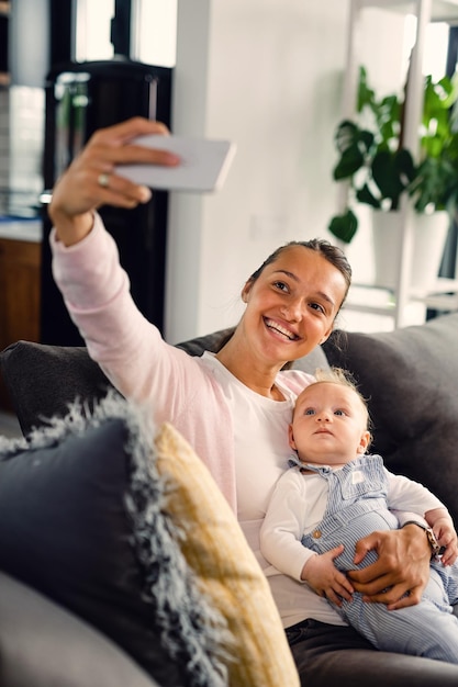 Photo young happy mother taking selfie with her baby boy and having fun in the living room