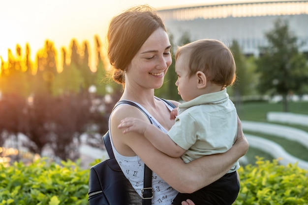 A young happy mother with a young son walks through the park on a summer day at sunset Concept of the joy of motherhood