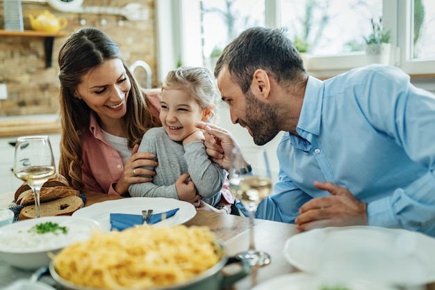 Young happy parents having fun with their small daughter during lunch time in dining room