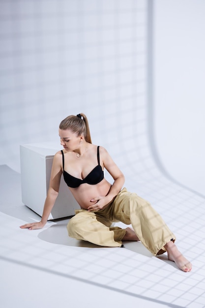 Young happy pregnant woman in bra and pants on white background Happy pregnancy Stylish pregnant woman poses in the studio