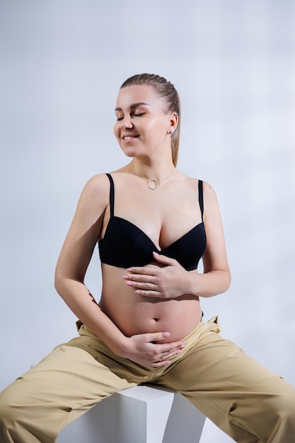 Young happy pregnant woman in bra and pants on white background Happy pregnancy Stylish pregnant woman poses in the studio