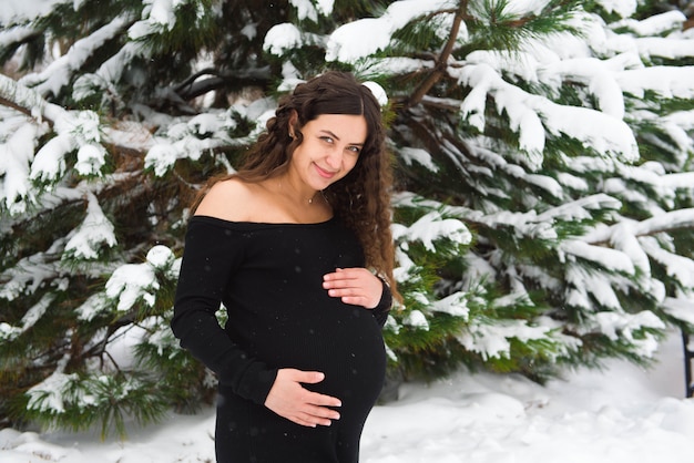 Young happy pregnant woman in snowy forest