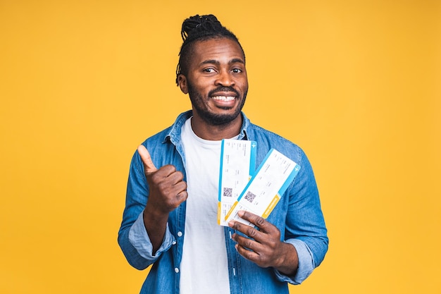 Young happy smiling African american black Man Holding Boarding Pass tickets isolated Over yellow Background.