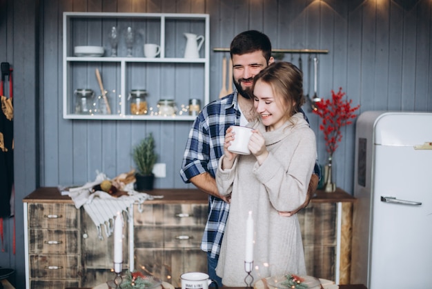 Young happy smiling cheerful couple hugging together in cozy christmas decorated kitchen.