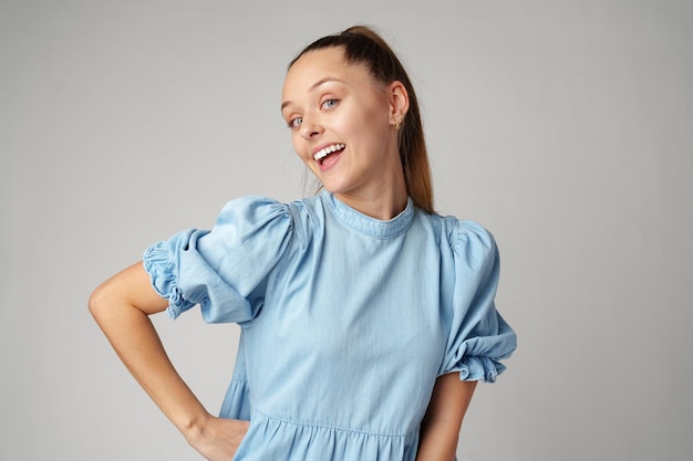 Young happy smiling woman in a light blue dress on a gray background