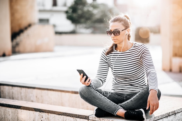 A young happy teen girl using a smart phone sititng in the city