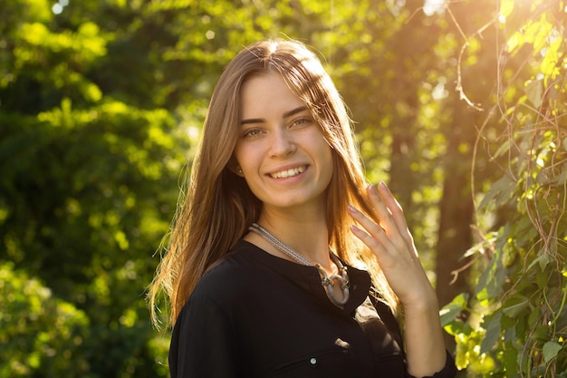 Young happy woman in black blouse touching her long hair on the background of green trees