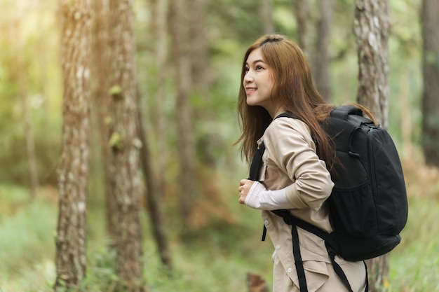 Young happy woman carrying a backpack travel and walking in the forest