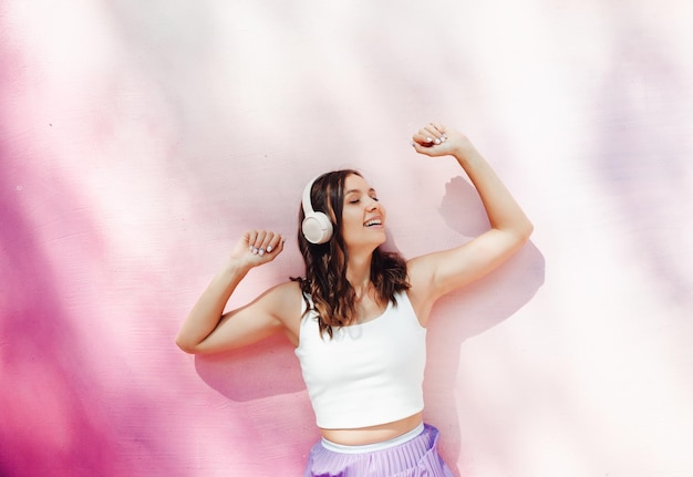 A young happy woman dressed in a white top and purple skirt headphones listening to music dancing on