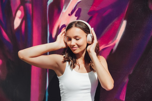 A young happy woman dressed in a white top and purple skirt headphones listening to music dancing on