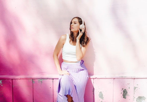 A young happy woman dressed in a white top and purple skirt headphones listening to music dancing