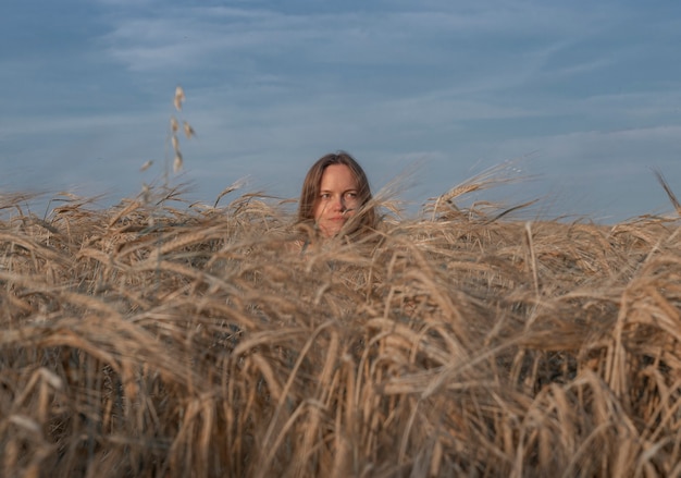 Young happy woman inside wheat field in summer natural light and cloudy sky