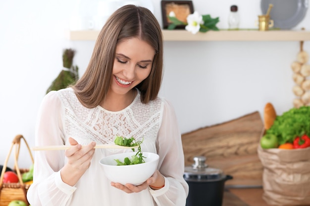 Young happy woman is cooking or eating fresh salad in the kitchen Food and health concept