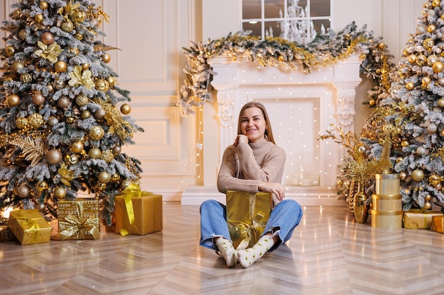 A young happy woman is sitting with a New Year's gift Christmas tree and fireplace with festive garlands New Year's mood