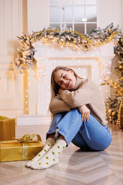 A young happy woman is sitting with a New Year's gift Christmas tree and fireplace with festive garlands New Year's mood