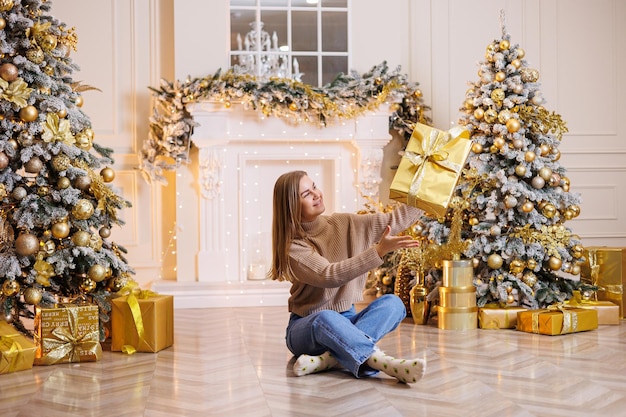 A young happy woman is sitting with a New Year's gift Christmas tree and fireplace with festive garlands New Year's mood