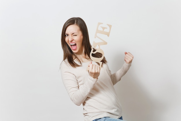 Young happy woman in light casual clothes holding wooden word love, doing winner gesture on white background. Copy space for advertisement. St. Valentine's Day or International Women's Day concept.