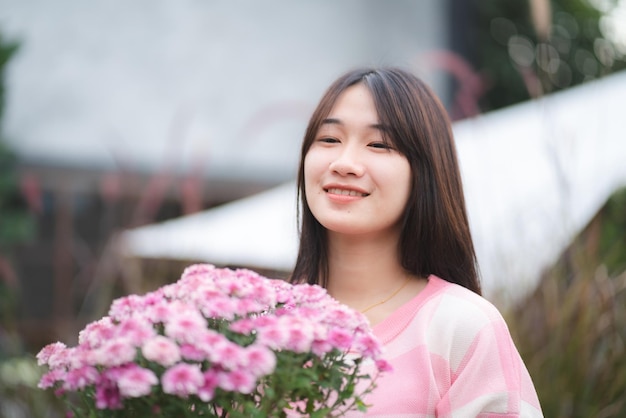 Young happy woman person smiling with pink flower blooming pretty cute girl portrait in summer with nature flower plant in pink color and colorful natural outdoor