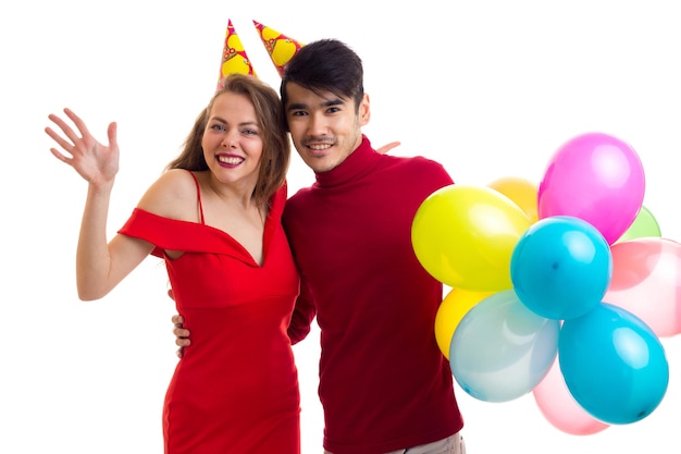 Young happy woman in red dress with colored hat and handsome man in red shirt blowing balloons