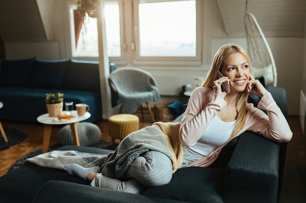 Young happy woman relaxing on the sofa and communicating with someone over mobile phone.