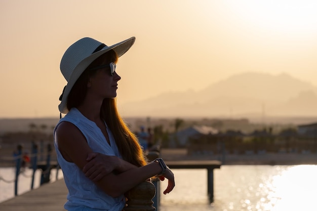 Young happy woman tourist relaxing outdoors on warm sunny evening on sea shore Summer vacations and travelling concept