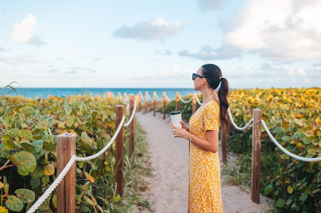 Young happy woman walking on the beach with coffee to go