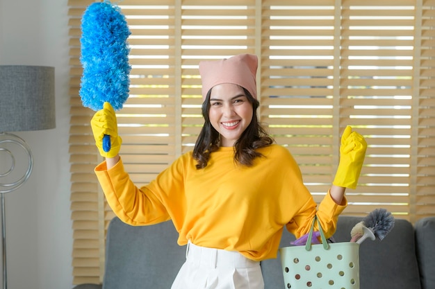 Young happy woman wearing yellow gloves and holding a basket of cleaning supplies in living room