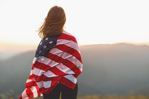 Young happy woman with flag of united states enjoying the sunset on nature