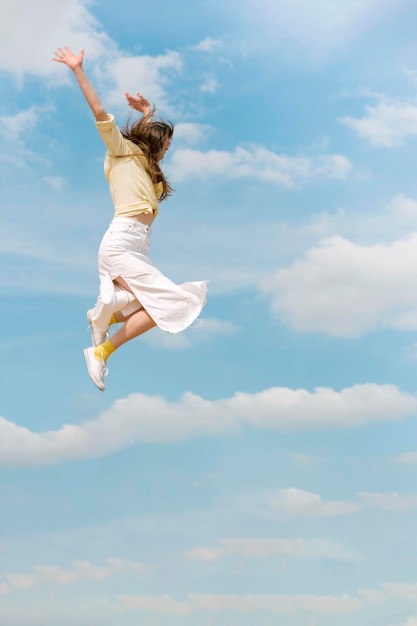 Young happy woman with her hands raised up during jump against the blue sky Young girl flying high in blue sky