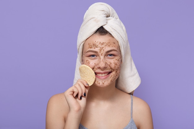 Young happy woman with moisturizing facial mask, holds sponge for removing makeup